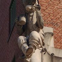 Carved stone gargoyle-style figure of a bulldog drinking from a beer stein, mounted on the exterior of the Anheuser-Busch brewery building.
