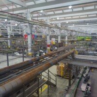 Rusted overhead pipes running through the Anheuser-Busch packaging facility, with Bottle Line 34 visible in the background.