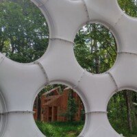 A second view through the circular openings of the Fly's Eye Dome toward a wooden art structure in the forest at Crystal Bridges.