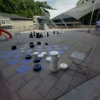 Giant outdoor chess and checkers pieces set up on a courtyard patio at Crystal Bridges Museum, with the museum's architecture visible in the background.