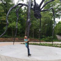 Nancy standing beneath the full span of Louise Bourgeois's giant spider sculpture Maman, showing its full scale.