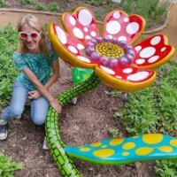 Nancy kneeling beside a large, colorful whimsical flower sculpture with polka-dot petals at Crystal Bridges Museum.