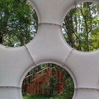 Looking through the circular openings of Buckminster Fuller's Fly's Eye Dome toward a wooden art structure in the forest at Crystal Bridges Museum.