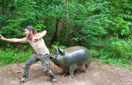 Zach dramatically pulling on the ear of a large bronze pig sculpture along a Crystal Bridges trail.