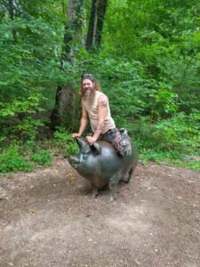 Zach sitting on top of a large bronze pig sculpture along a wooded trail at Crystal Bridges Museum.