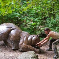 Zach touching a bronze bear sculpture resting in the woods along a Crystal Bridges trail.