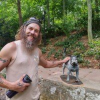 Zach petting a small dog sculpture along a wooded trail at Crystal Bridges Museum.