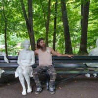 Zach sitting among ghostly white plaster figure sculptures on a park bench at Crystal Bridges Museum.