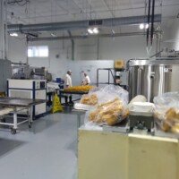 Factory production room with clear bags of golden candy pieces in front and two workers in white coats at a table in the back