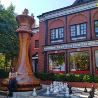 Zach sitting on the base of the 20-foot World's Largest Chess Piece outside the World Chess Hall of Fame in St. Louis, next to a giant outdoor chessboard